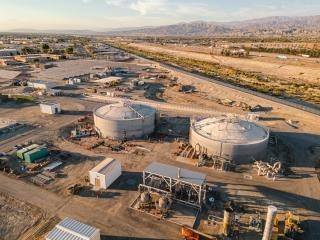 Industrial site with large storage tanks, various structures, and open land under a clear sky.