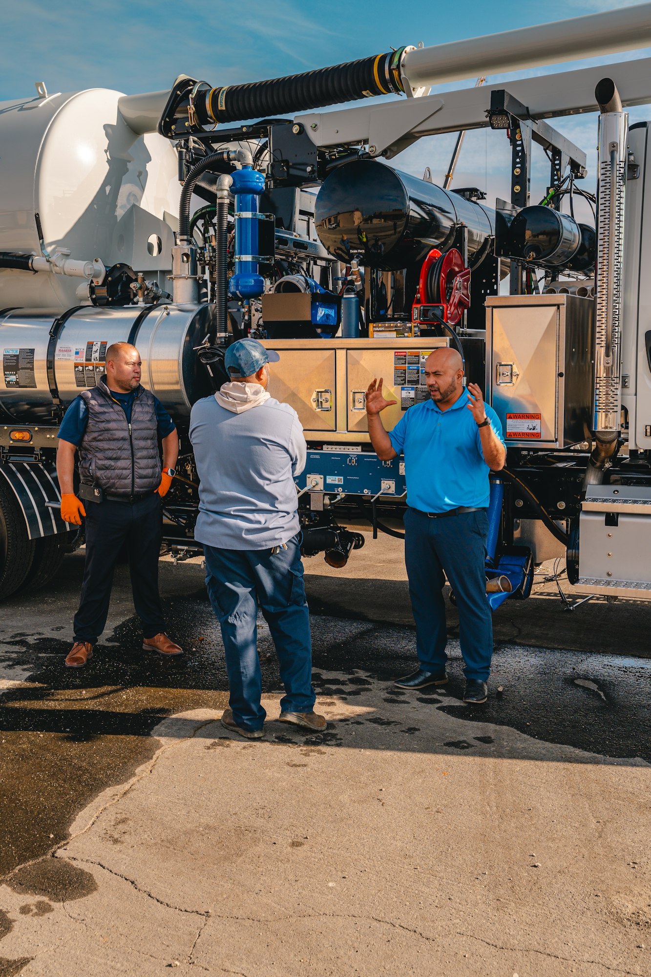 Three people discussing beside industrial equipment on a truck, with one person gesturing.