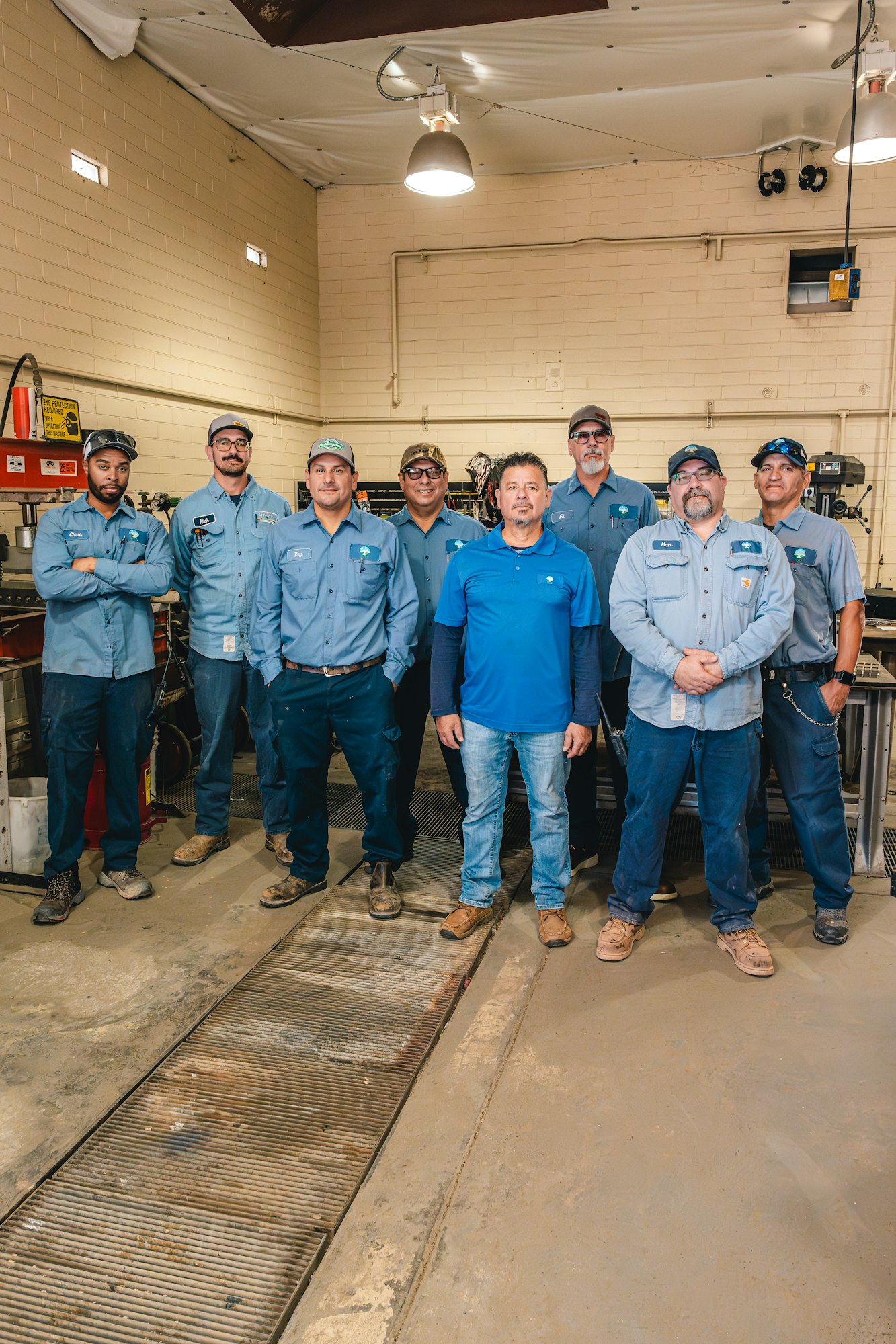 A group of eight men in work uniforms standing in a workshop.