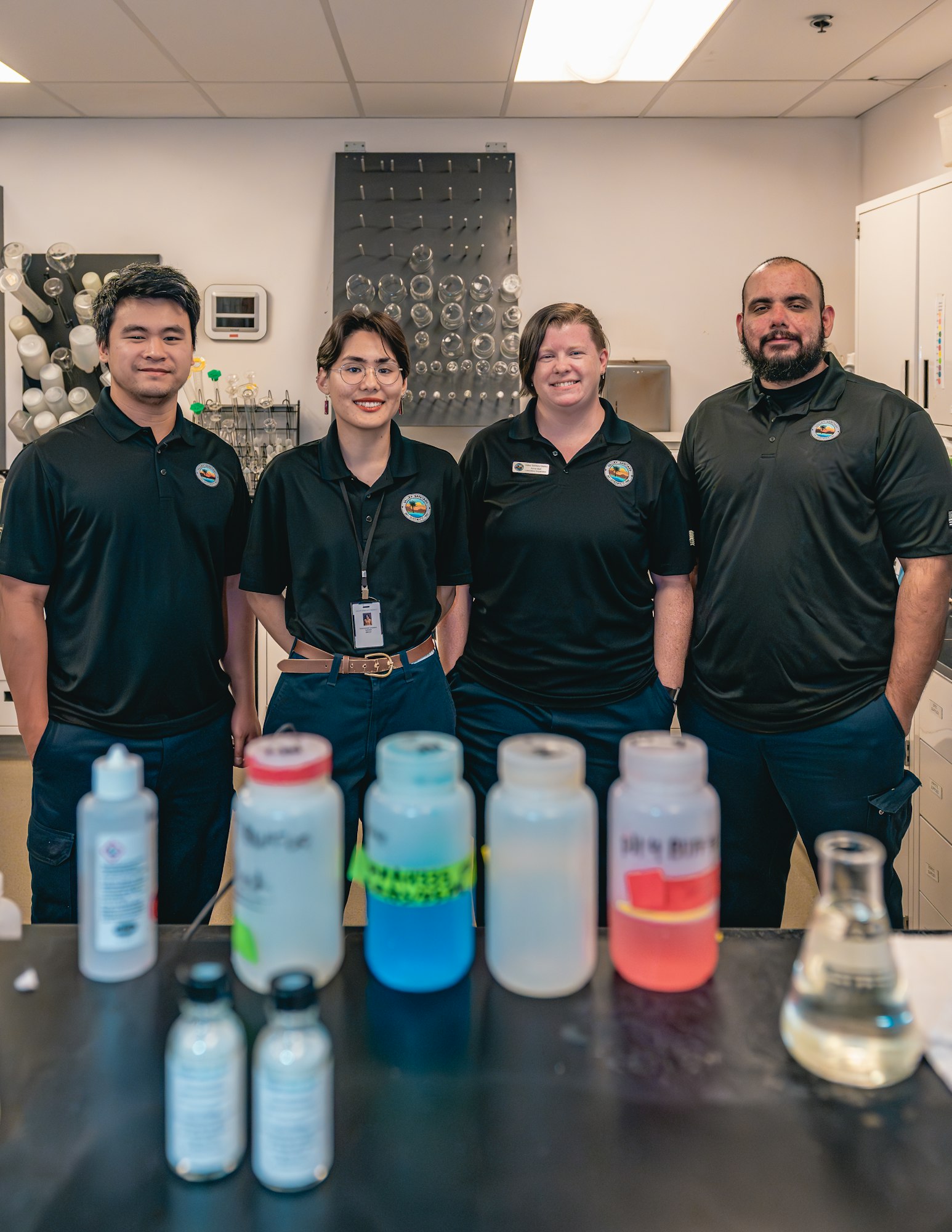 Four people in a lab stand behind a table with bottles and equipment.