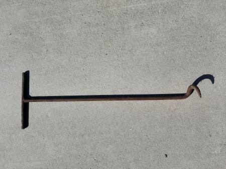 A rusty metal T-handled tool with a curved hook on one end, lying on a concrete surface.