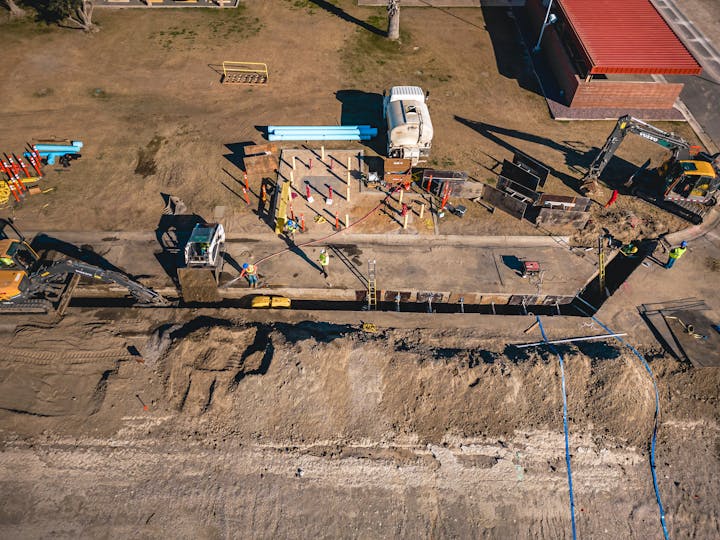 Construction site with machinery, workers, and dug trenches, viewed from above.