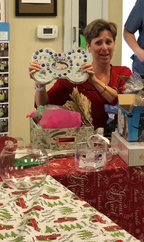 A woman holds a decorated bone-shaped plaque labeled "Ginger," surrounded by festive wrapping paper and gifts.