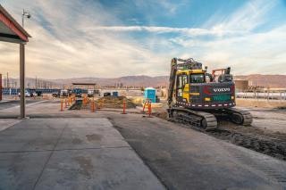 A construction site with an excavator, orange cones, and a porta-potty under a partly cloudy sky.