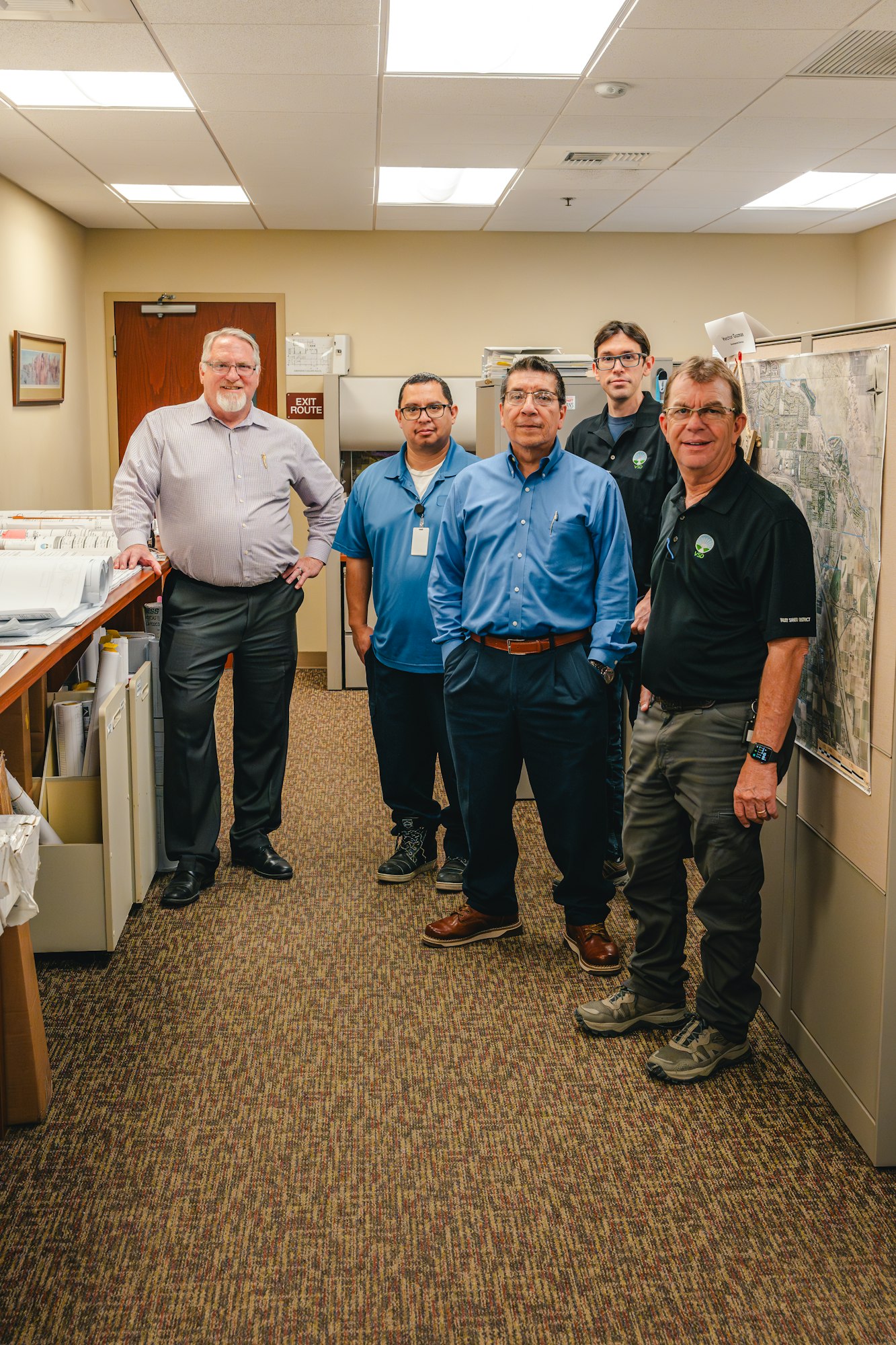 Five men standing in an office with maps and documents around them.