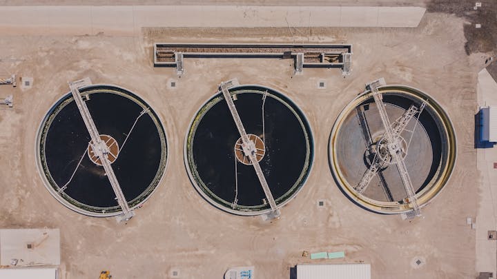 Three circular water treatment tanks with overhead walkways, viewed from above in an industrial setting.