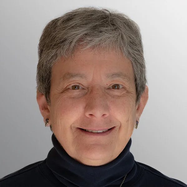 A person with short gray hair, wearing a black turtleneck, smiling against a light background.