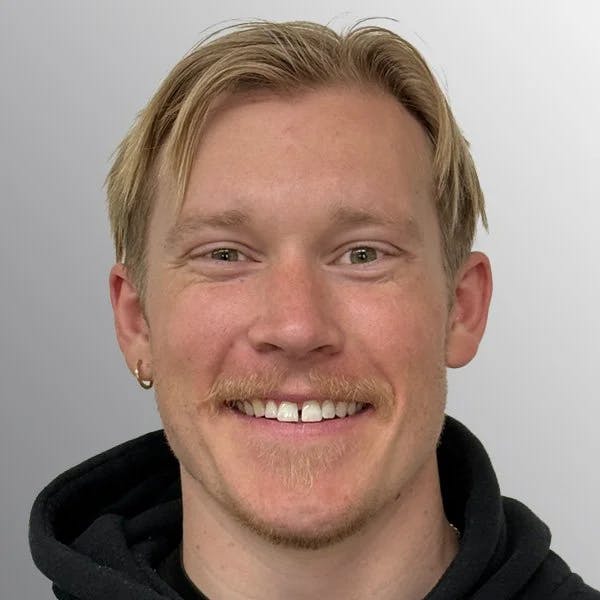 A person with short blond hair and a mustache is smiling at the camera.
