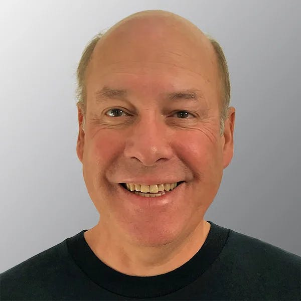A smiling man with a bald head and a dark shirt against a light gray background.