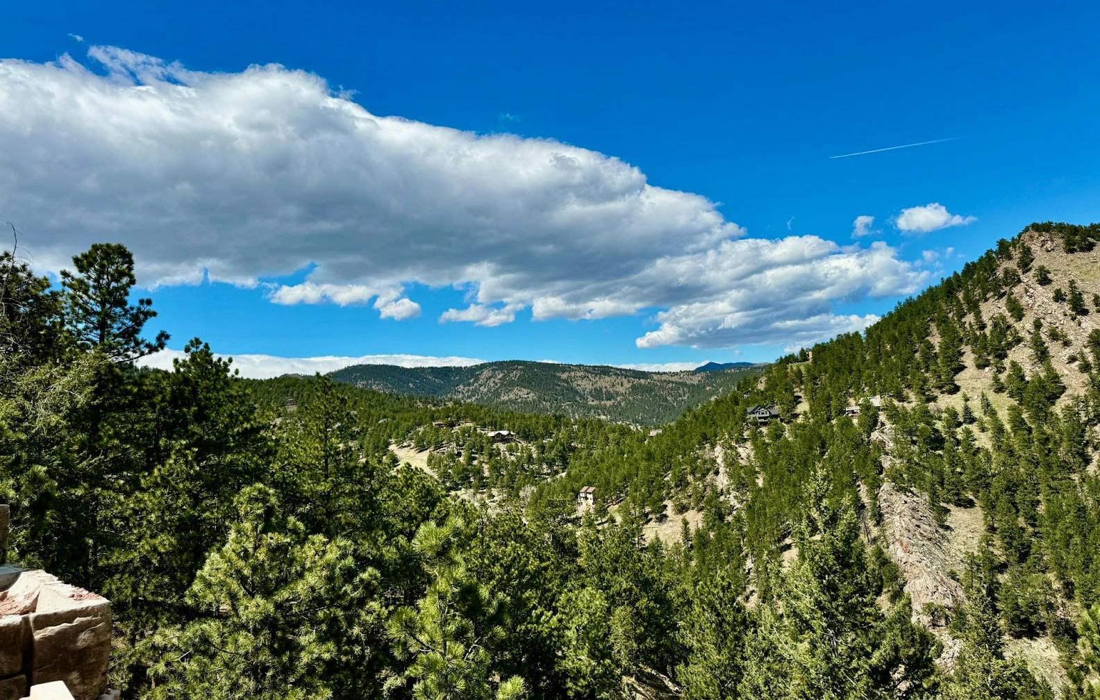 A scenic view of forested hills under a blue sky with scattered white clouds.