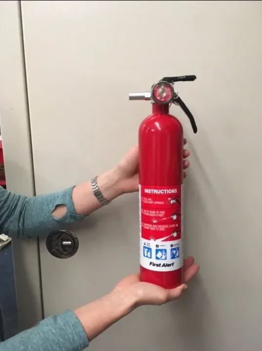 Person holding a red fire extinguisher with instructions on the label.