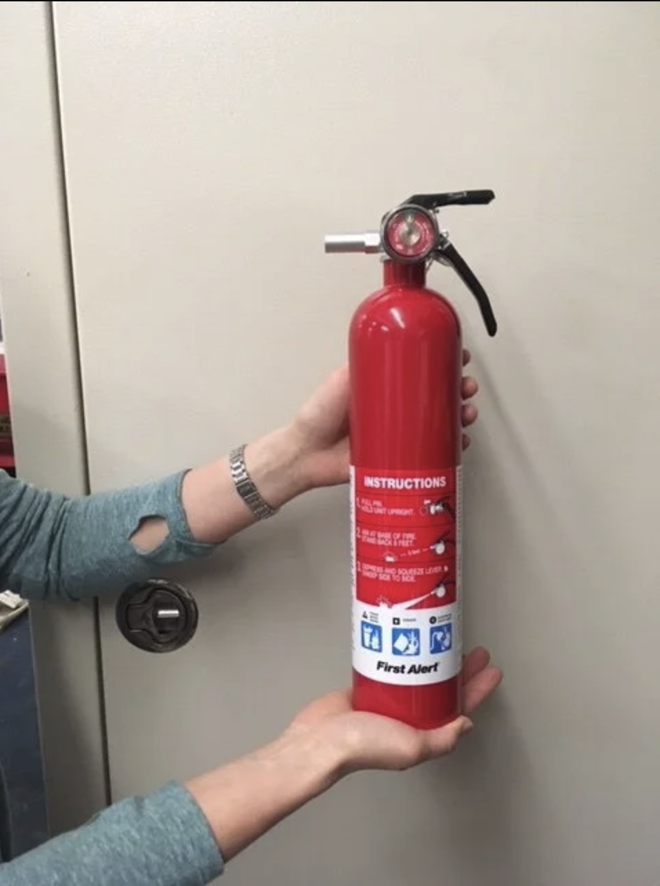 Person holding a red fire extinguisher with instructions on the label.