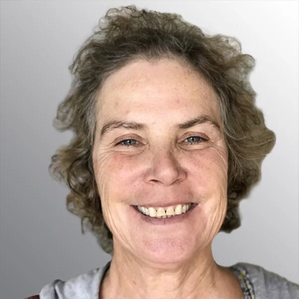 A person smiling with short, curly hair against a light gray background.