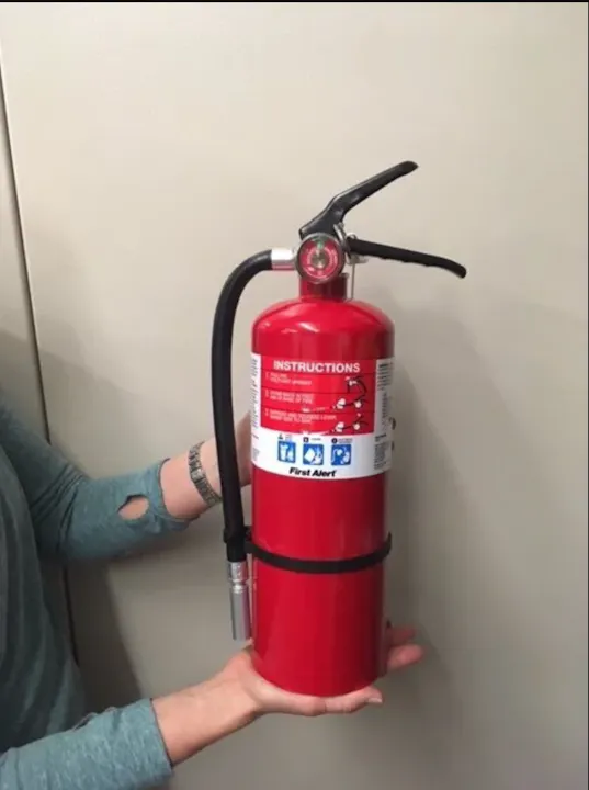 A person is holding a red fire extinguisher labeled "First Alert" with instructions visible.