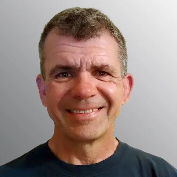 A person smiling at the camera with a neutral background.