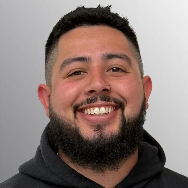 A smiling man with a beard and a nose ring, wearing a dark hoodie.