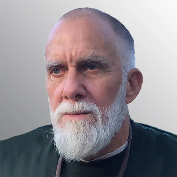 An older man with a white beard wearing a dark shirt, against a light background.