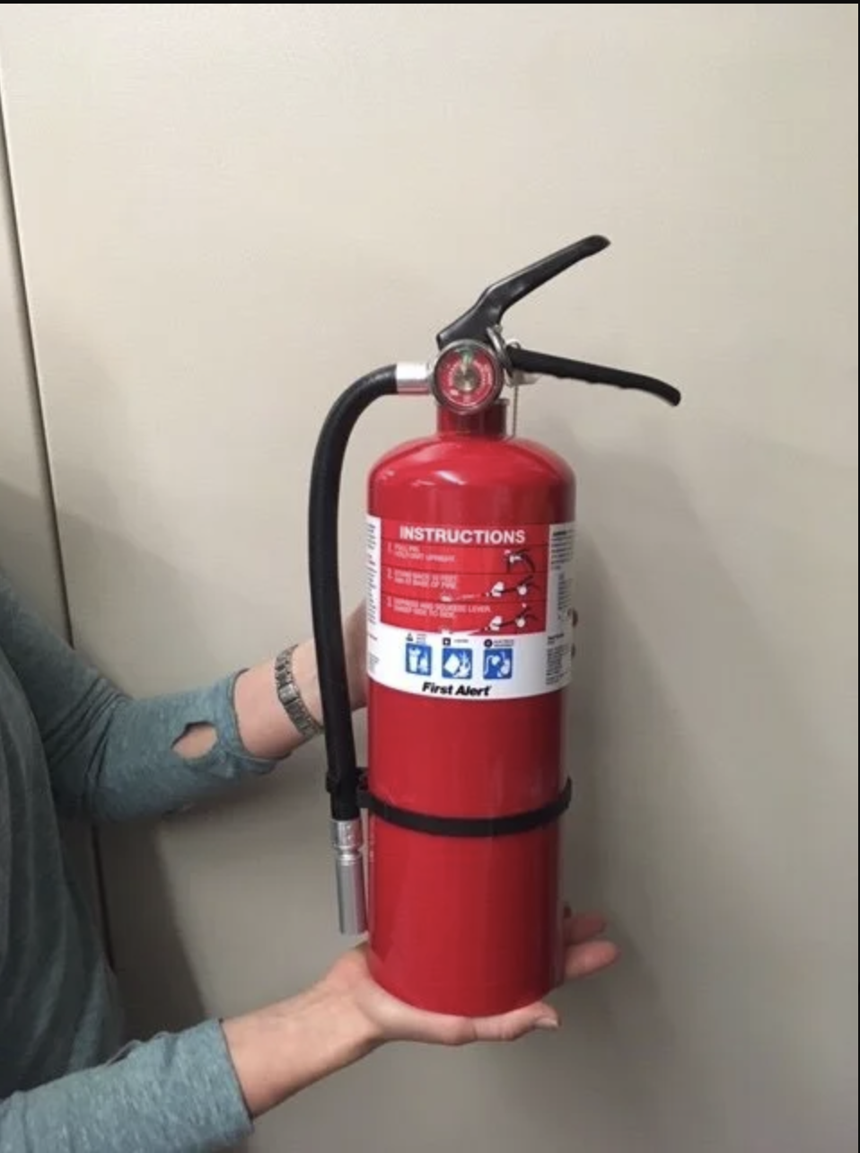 A person holding a red fire extinguisher with visible instructions.