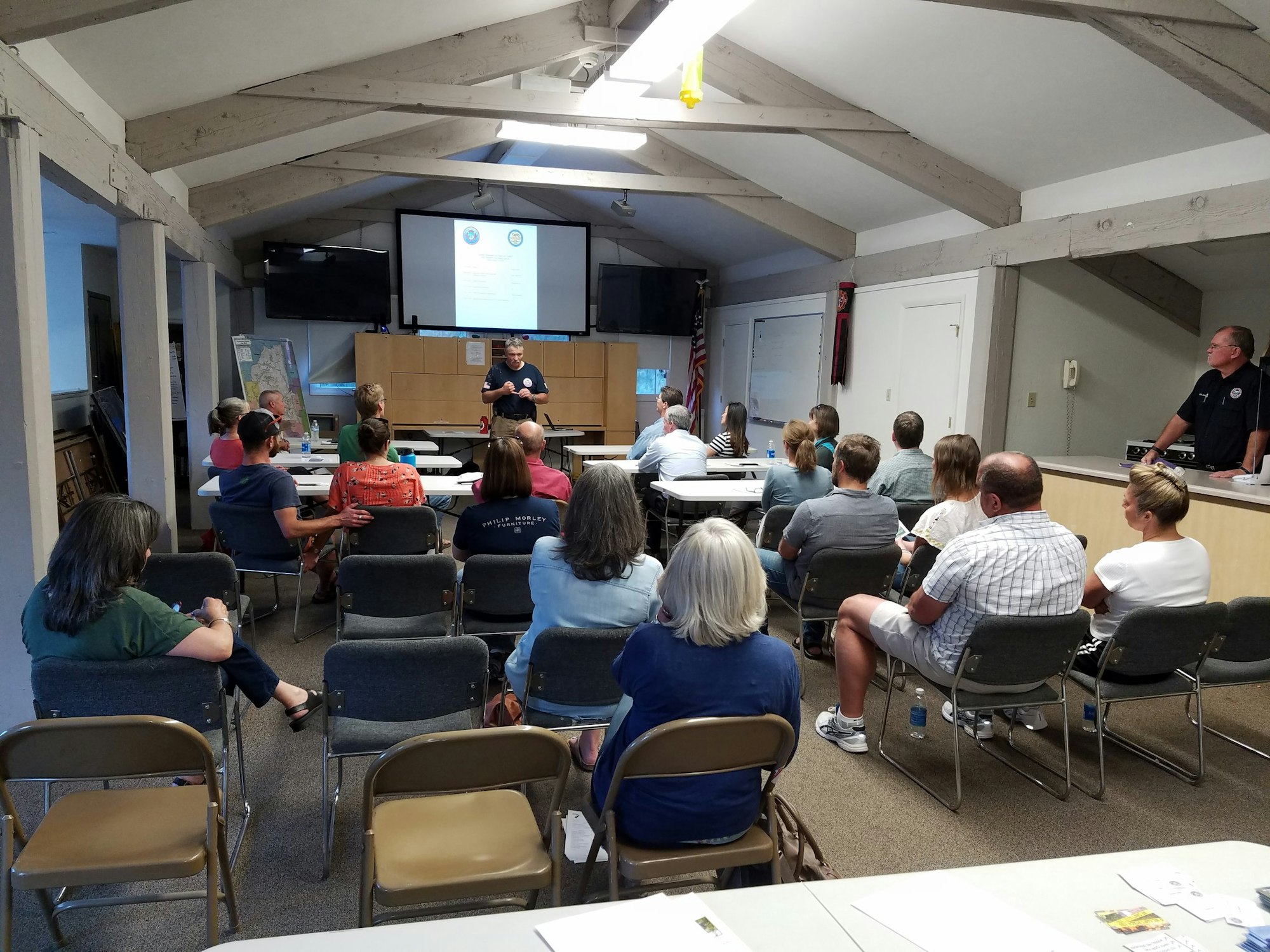 A group of people is attending a presentation or meeting in a room with a screen and chairs.