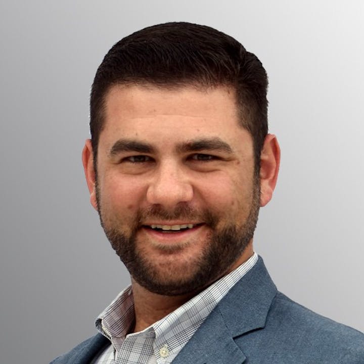 A man in a suit smiling against a gray background.