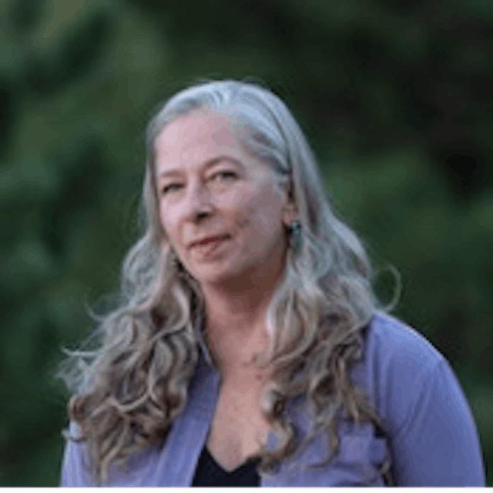 A person with long gray hair in a purple shirt, outdoors.