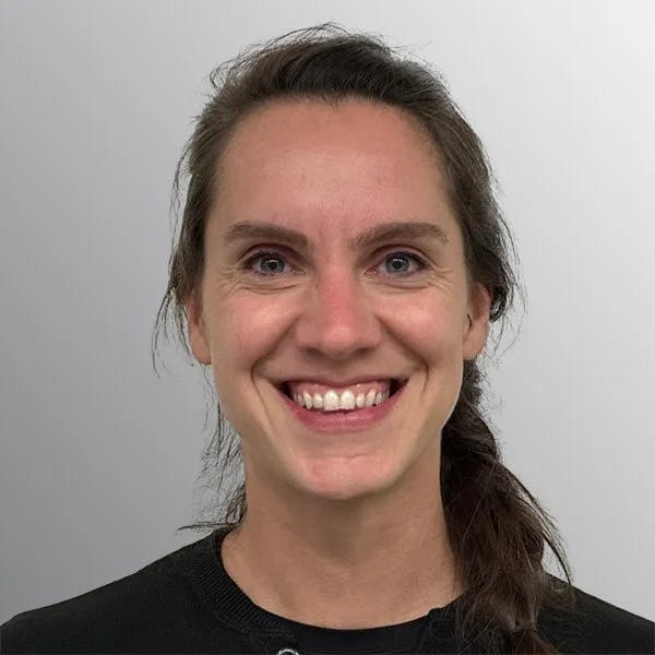 A person with dark hair smiling against a light gray background.
