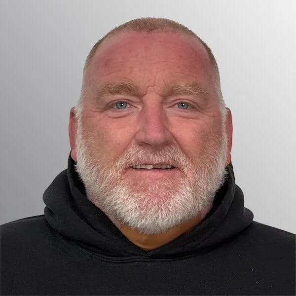 A man with a beard, wearing a black hoodie, against a gray background.