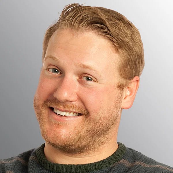 A smiling person with short, light brown hair, wearing a striped sweater against a gray background.
