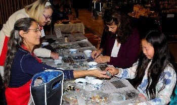 Four people sit at a table engaging in a craft activity involving small objects and beads.