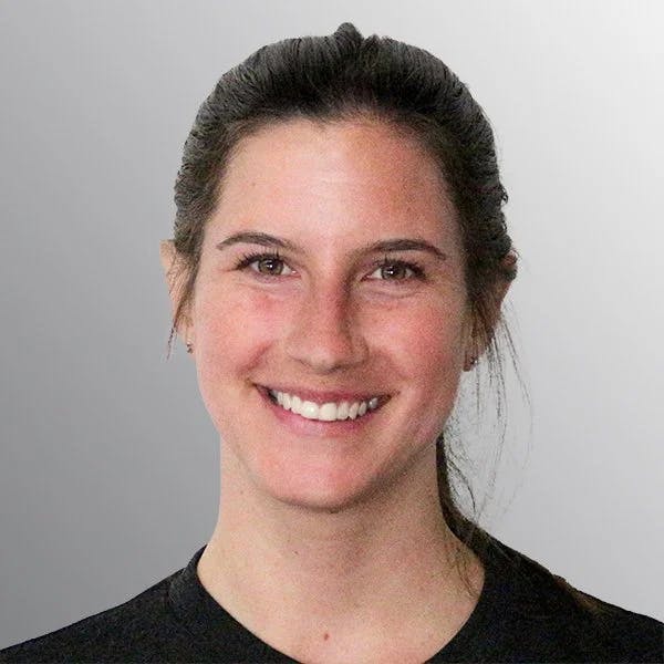 A person with tied-back hair smiles at the camera against a gray background.
