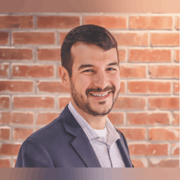 Smiling person in a blazer standing in front of a brick wall background.