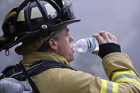 A firefighter in gear drinks from a water bottle, taking a moment to hydrate.