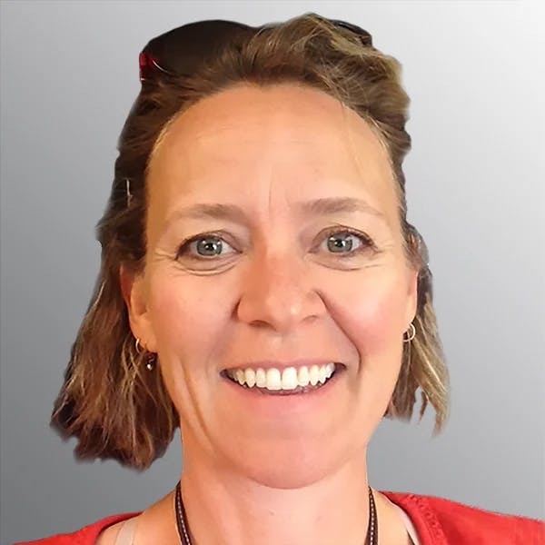 A person smiling with sunglasses resting on their head, against a neutral background.