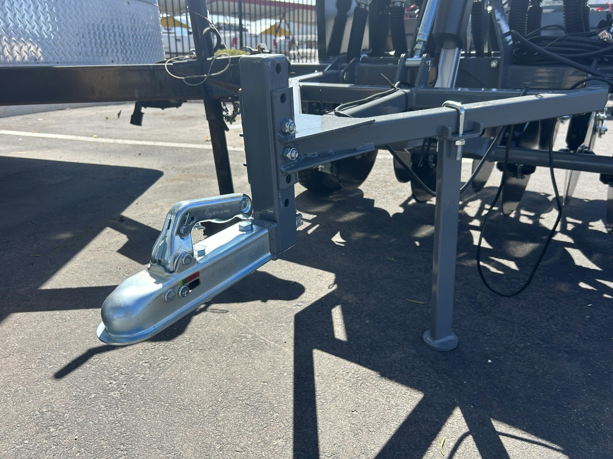A metal trailer hitch mechanism attached to a frame on a paved surface.