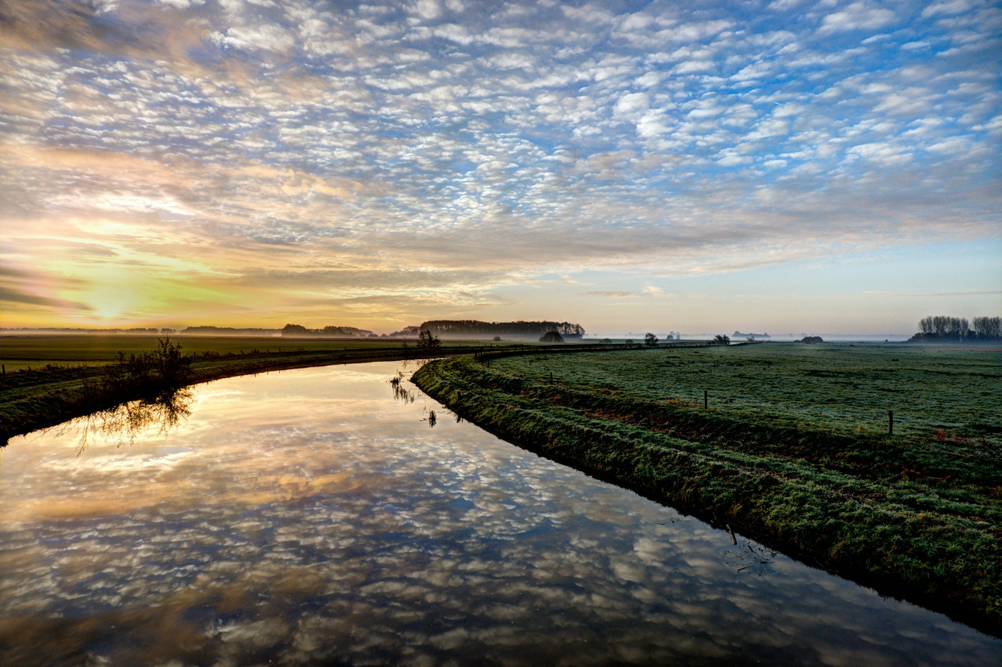 A serene landscape at sunrise, featuring a winding river reflecting colorful clouds and a frosty green field.