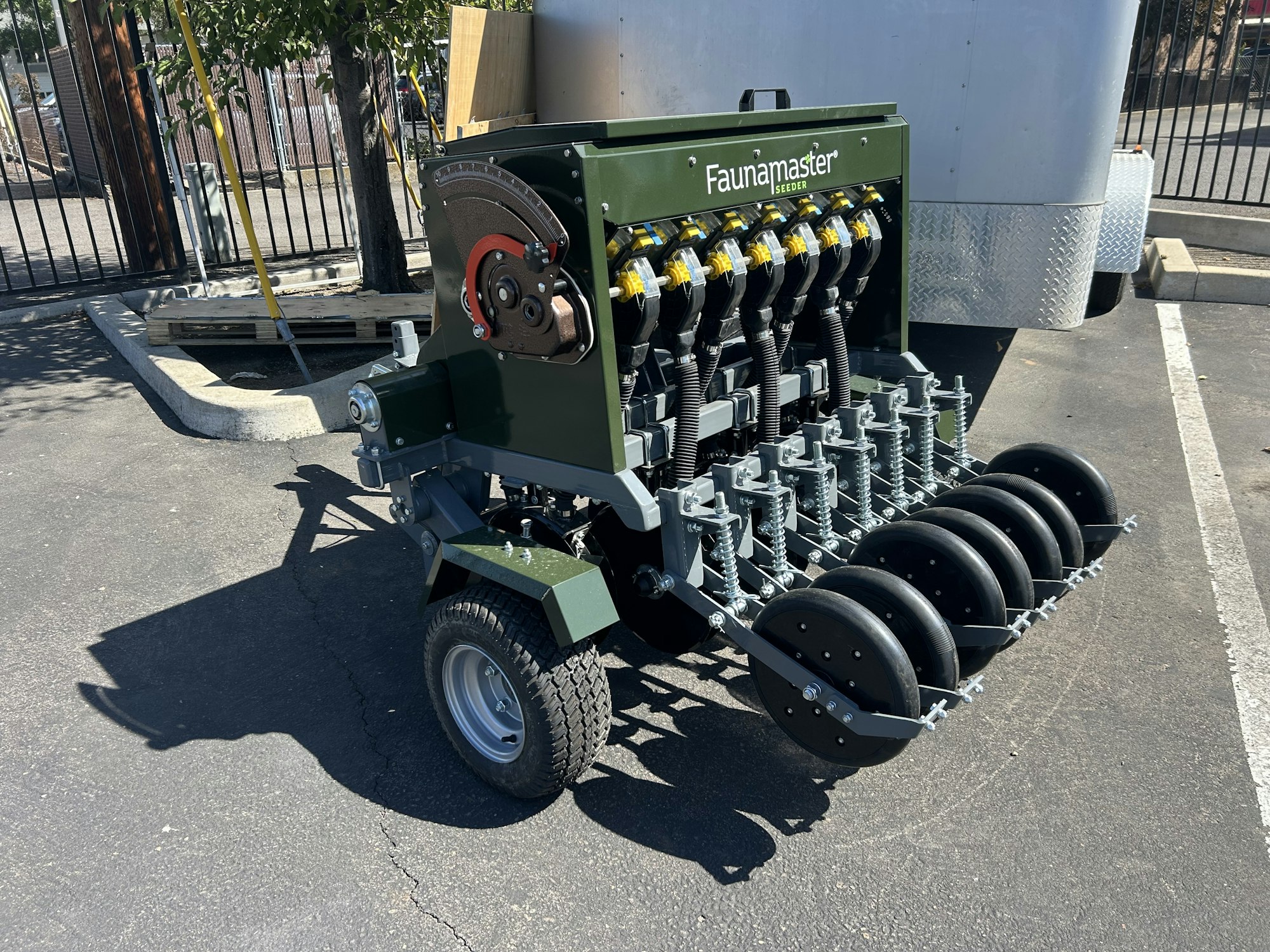 A Faunamaster Seeder is parked on a paved lot, featuring multiple seed dispensing mechanisms and wheels.