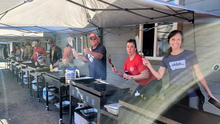People cooking on grills under tents, some with utensils and drinks, displaying various expressions.