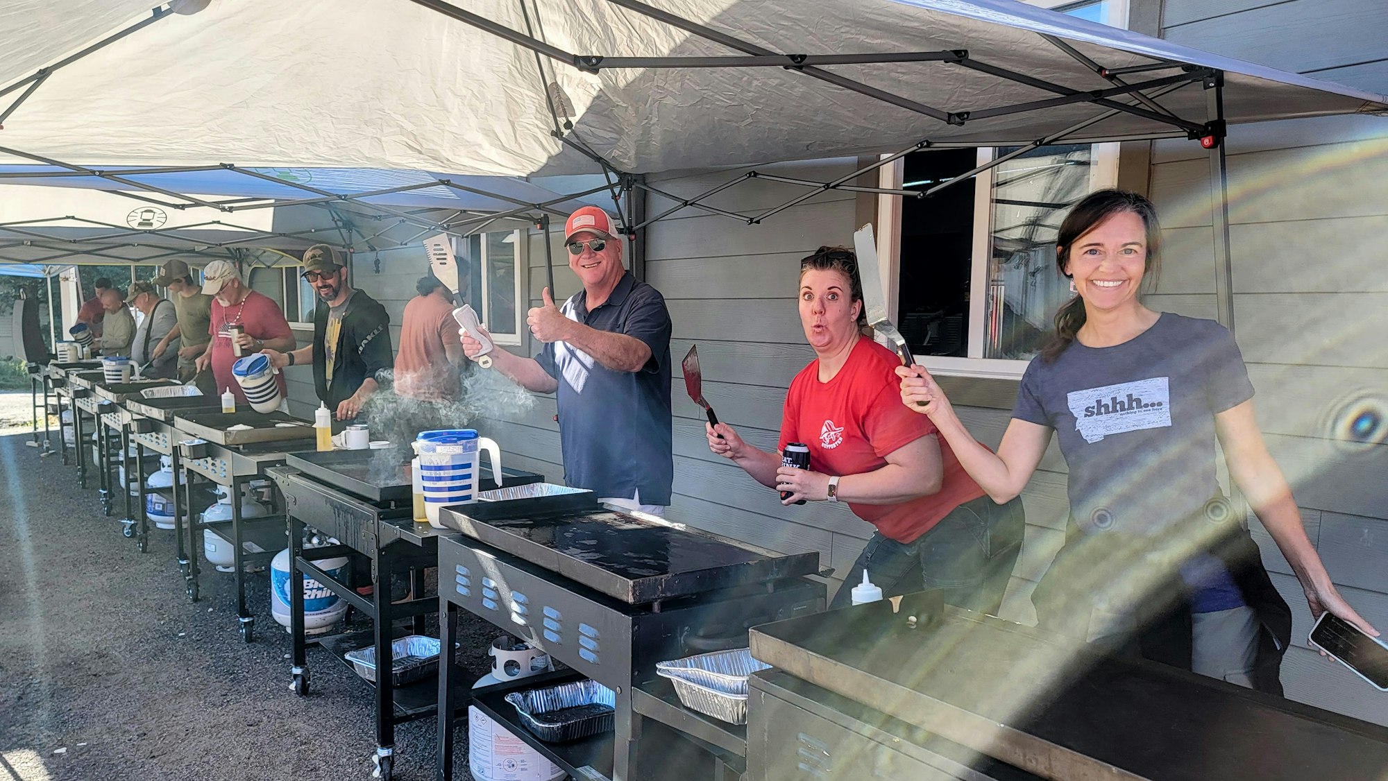 People cooking on grills under tents, some with utensils and drinks, displaying various expressions.