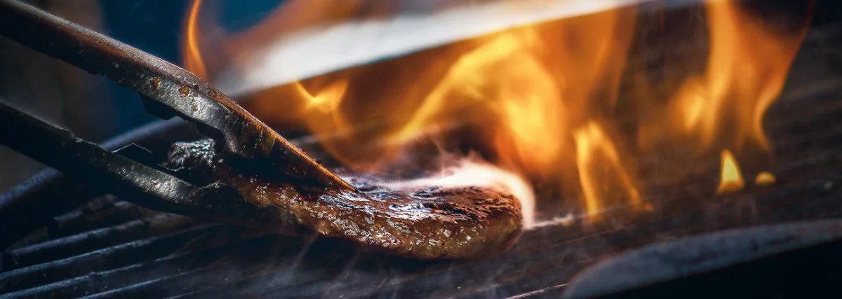 tongs turning burger on grill