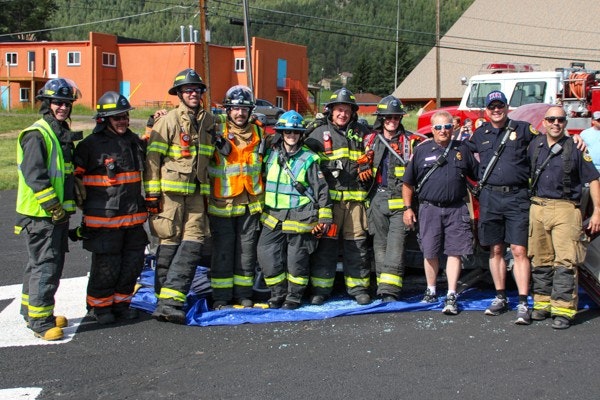 A group of firefighters in uniform posing together outdoors in a sunny setting.