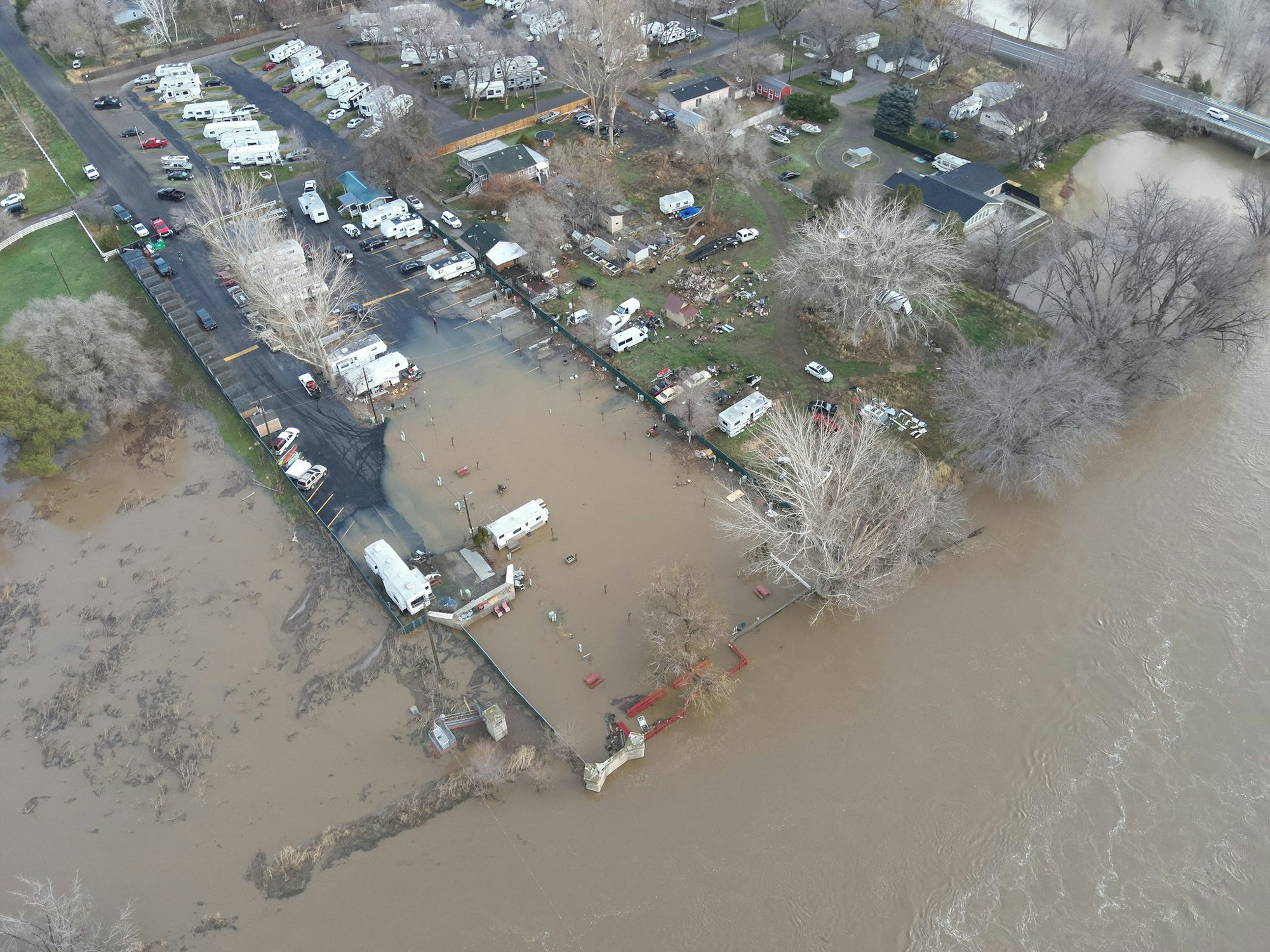 An aerial view of a flooded area with RVs and buildings submerged in rising water, indicating significant flooding.