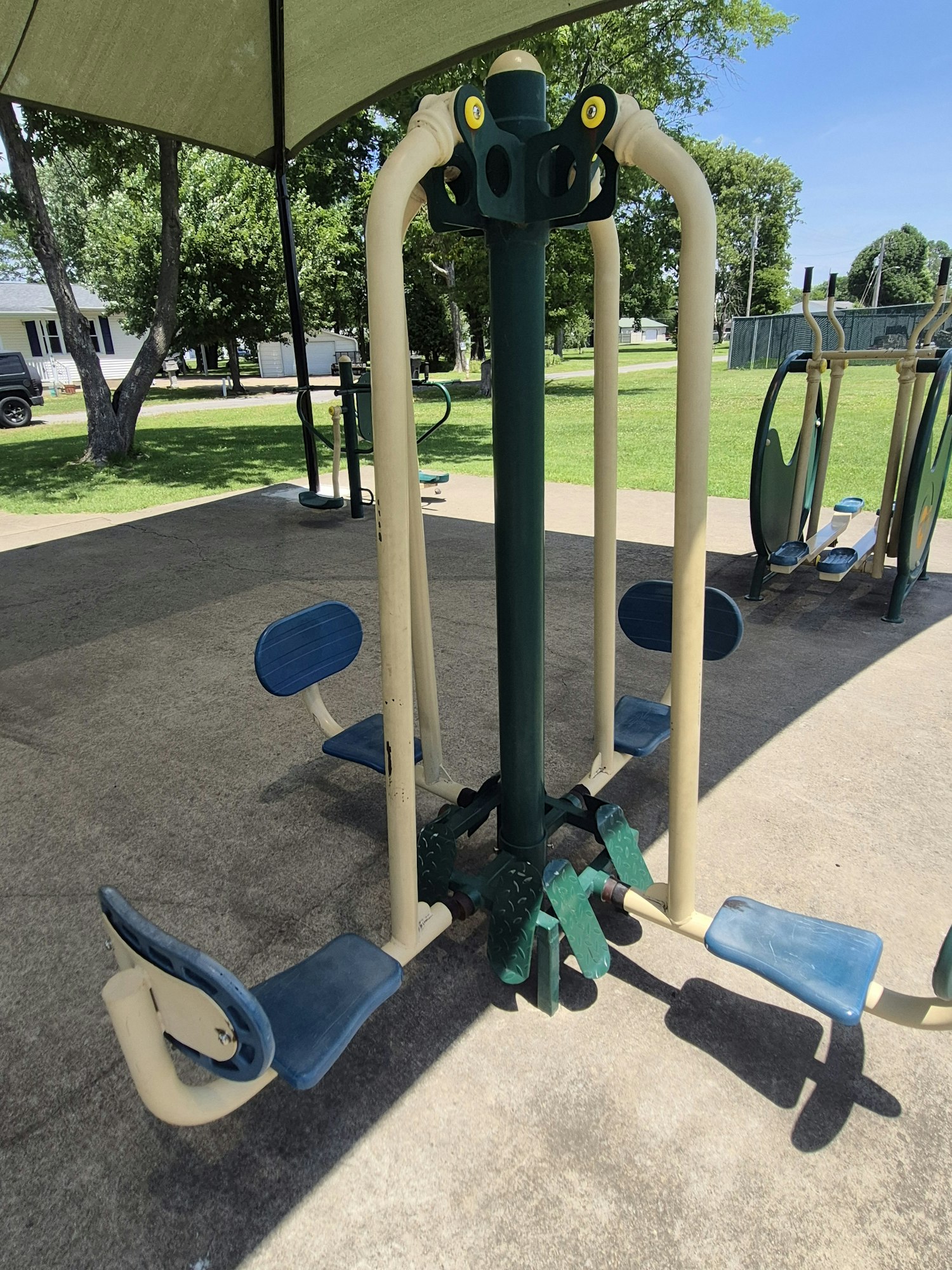 An outdoor exercise station with various equipment attached to a central post, set in a grassy park area.