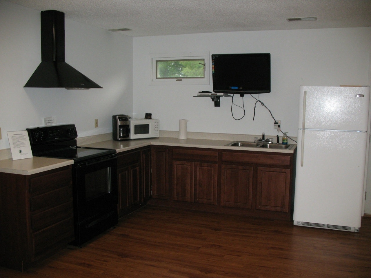 The image shows a modern kitchen with a black stove, white refrigerator, microwave, sink, and a mounted TV.