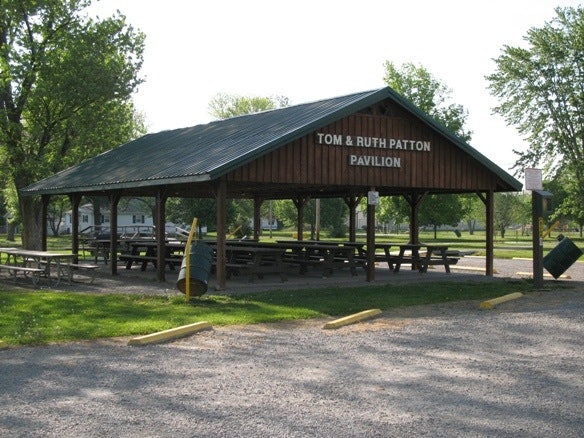 Image shows a wooden pavilion named "Tom & Ruth Patton Pavilion" with benches, surrounded by greenery and gravel.