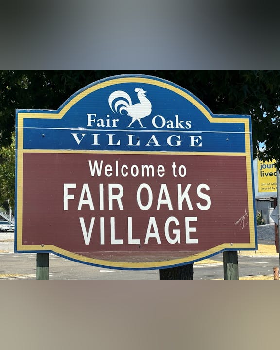 A sign saying "Welcome to FAIR OAKS VILLAGE" with a rooster symbol on top.
