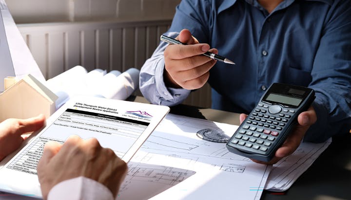 Two people discussing over architectural plans; one holds a calculator, the other a document.