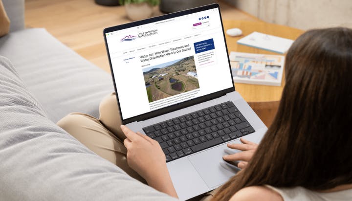 A person using a laptop, reading an article about water treatment and distribution from a website.