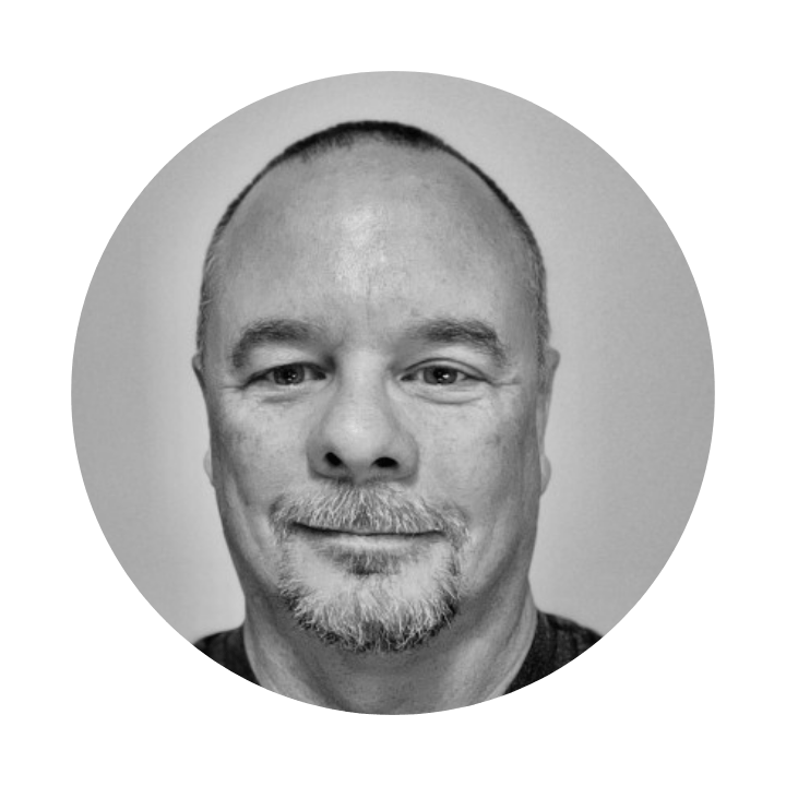 A black-and-white portrait of a smiling man with a goatee, set within a circular frame.