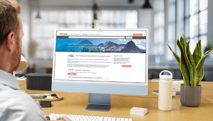 A person sits at a desk viewing a bid opportunities webpage on a monitor.
