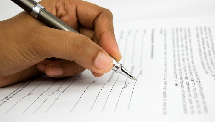 A person signing a document with a pen.